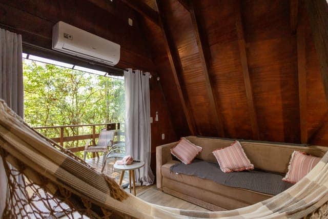 Interior de chalé com rede, ar-condicionado e vista para a mata